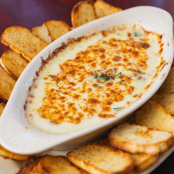 Grace's Place Pizzeria's baked spinach dip with melted cheese, served with toasted bread slices.