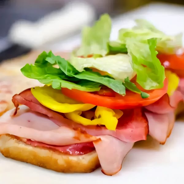 Close-up of a Grace's Place Pizzeria sub sandwich with ham, salami, lettuce, tomatoes, and peppers.