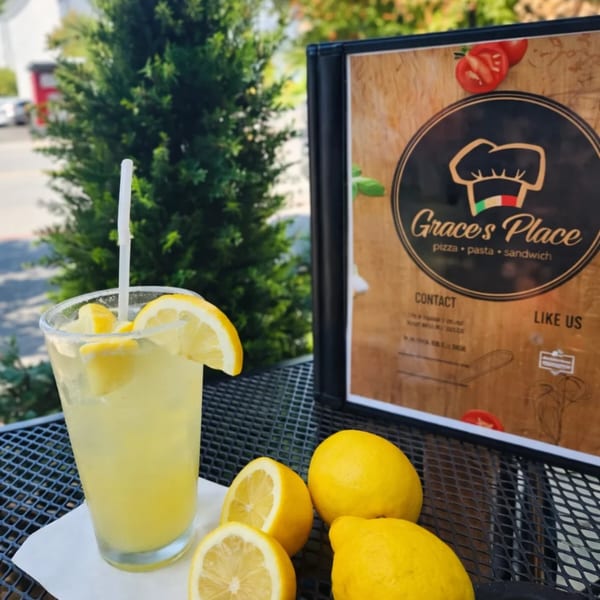 Lemonade with fresh lemons on an outdoor table next to a Grace's Place Pizzeria menu.